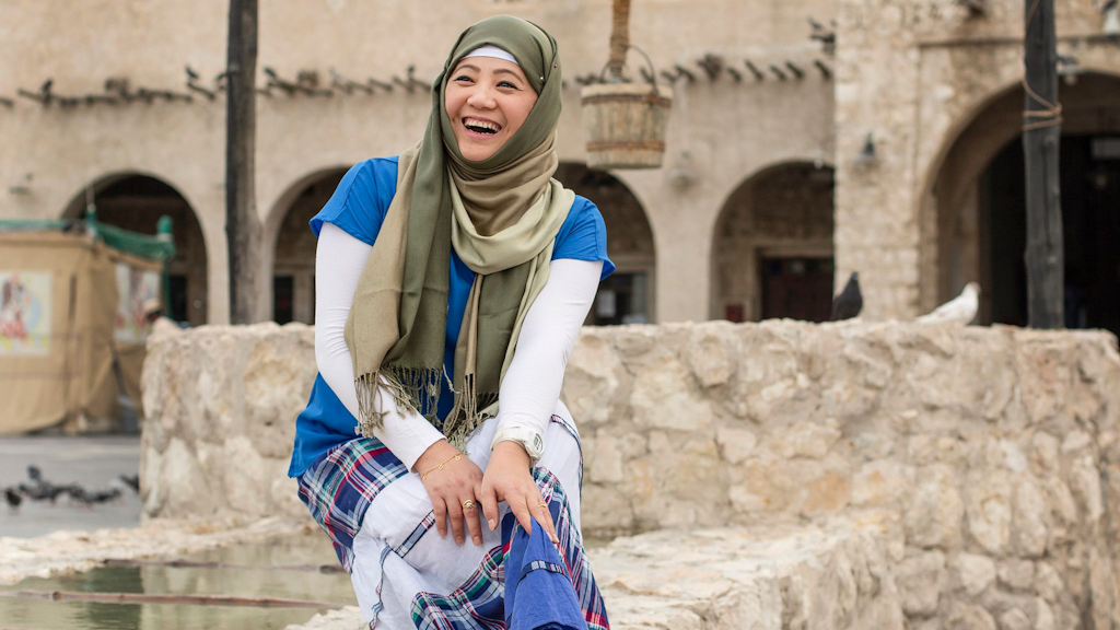 A woman sitting on a stone wall and laughing into the camera.
