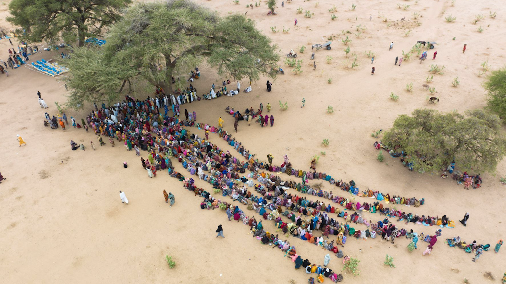 Birdseye view of many rows of people waiting in the desert to be registered.