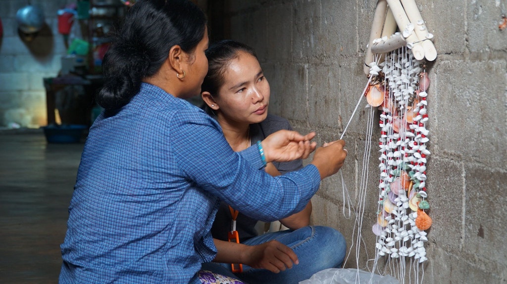 One woman showing another woman how to make an altar out of beads and shells